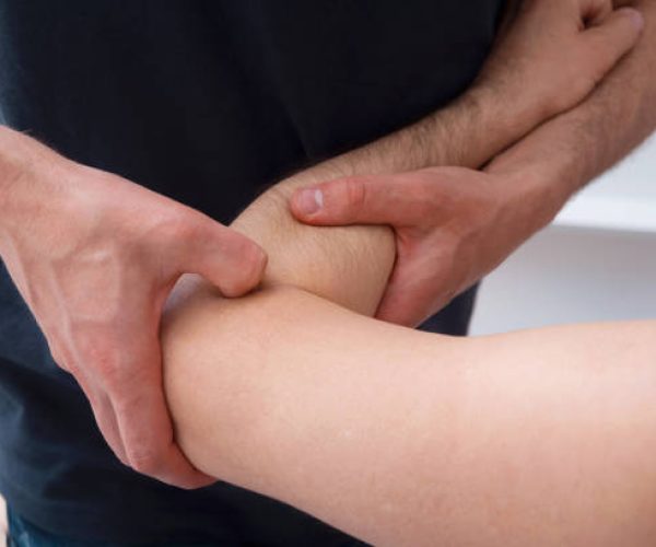 Male Physical therapist is pressing on one mans elbow making deep massage.